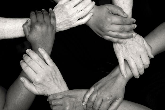 A black-and-white image of diverse hands interlocked in a supportive circle symbolising inclusivity.