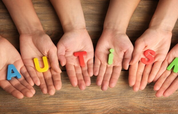Hands holding colorful letters spelling "AUTISM" on a wooden surface, symbolizing unity and support towards understanding autism.