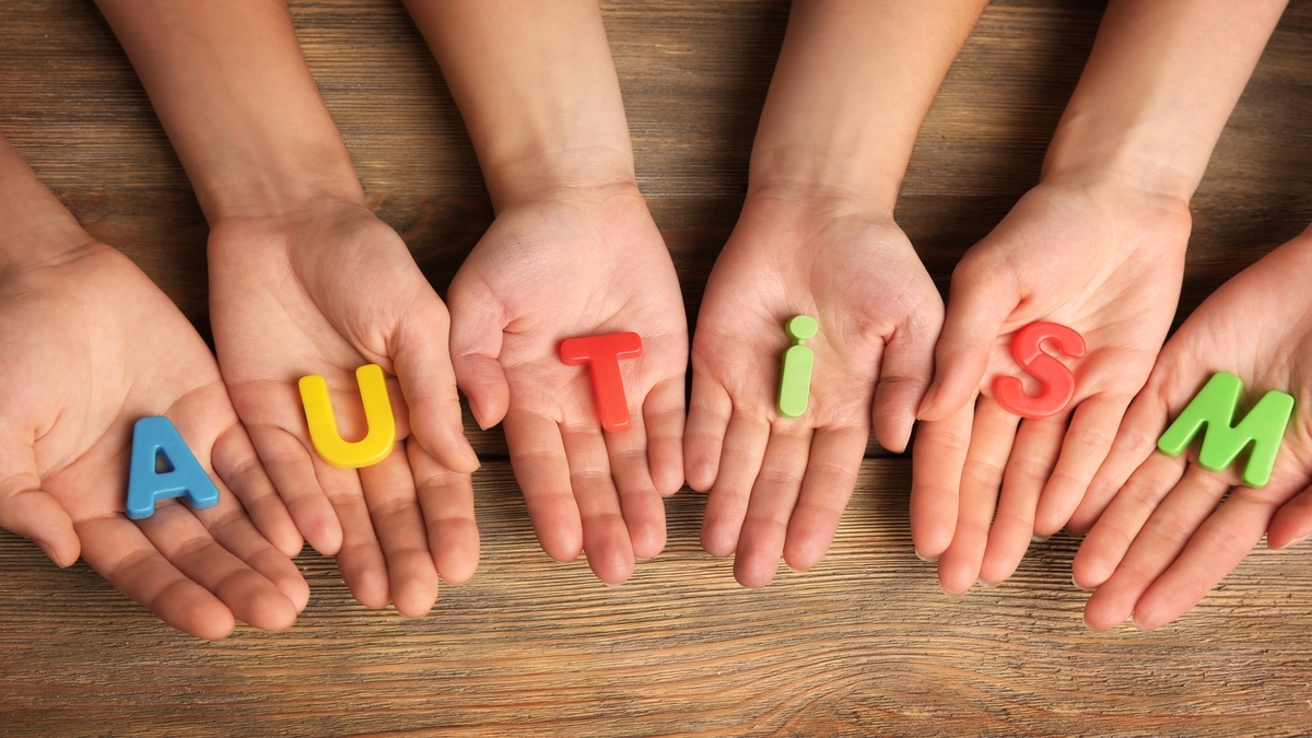 Hands holding colorful letters spelling "AUTISM" on a wooden surface, symbolizing unity and support towards understanding autism.