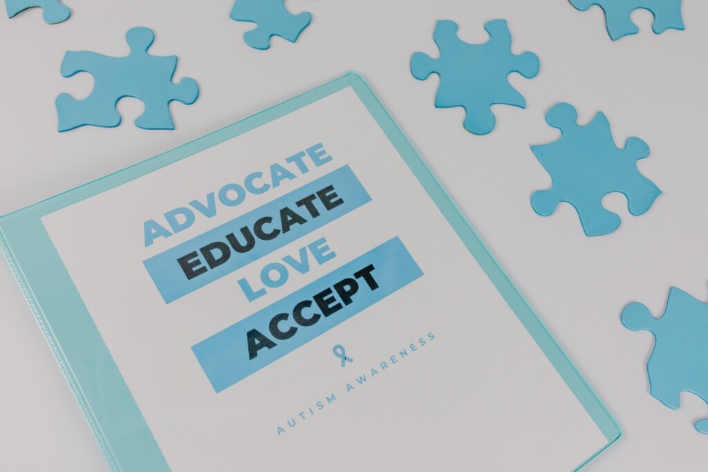 A binder with the words "Advocate, Educate, Love, Accept" surrounded by blue puzzle pieces.