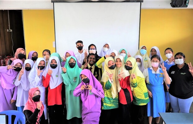 A group of trainers and schoolgirls wearing uniforms pose with peace and mini heart signs.