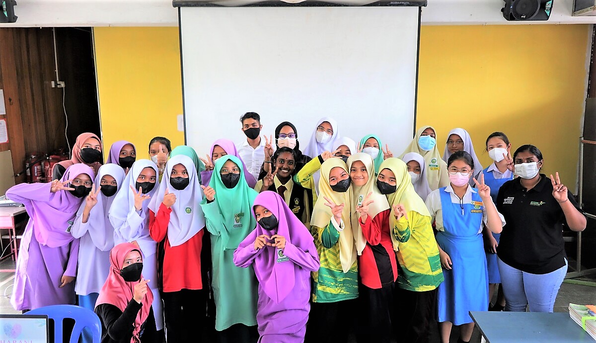 A group of trainers and schoolgirls wearing uniforms pose with peace and mini heart signs.
