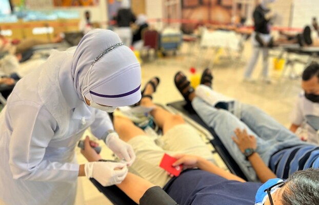 A nurse in uniform attentively assists a blood donor during a donation.
