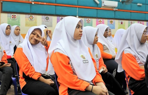 Two schoolgirls make cheeky faces among a group seated in an auditorium, engaged in an event.
