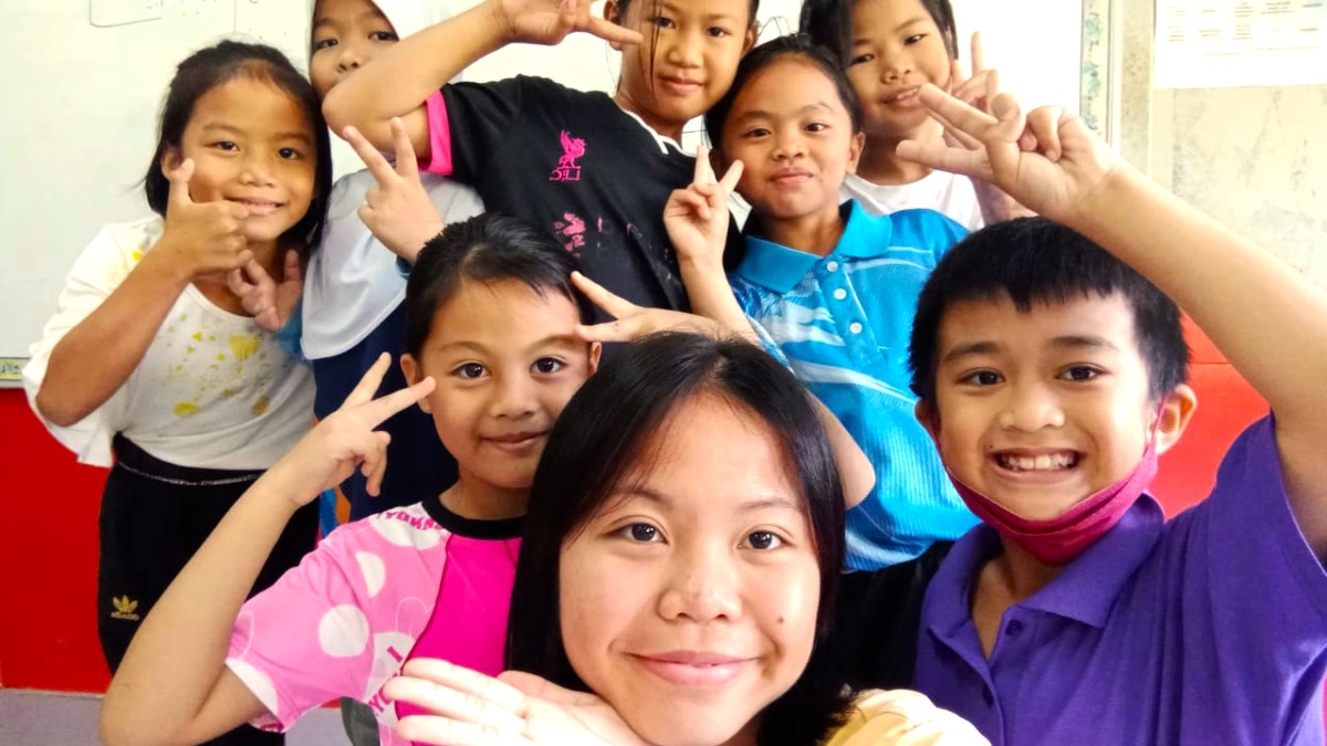 A young woman stands with a group of children as they smile and pose for a photo.