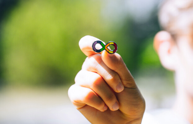A child holds an Autism infinity rainbow symbol in their hand.