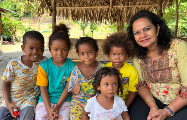 A woman sits smiling alongside a group of Orang Asli children in Baling, Kedah, capturing a moment of togetherness.