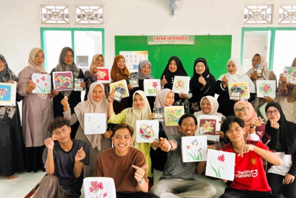 A group of smiling individuals holding up artwork featuring colourful floral designs, posing together in a cheerful atmosphere.