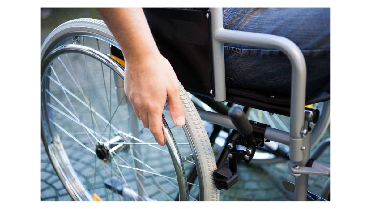 A person sitting in a wheelchair, with one hand visible gripping the wheel.