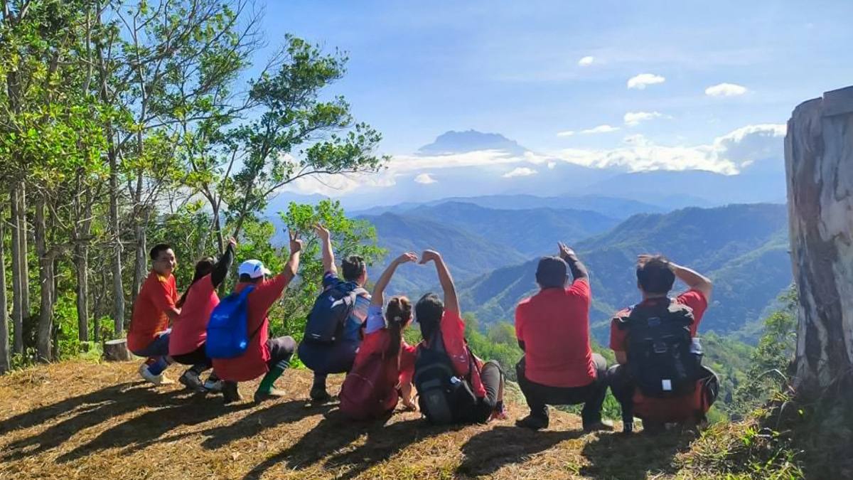 A group of trekkers squat facing a picturesque view of mountains in Sabah.