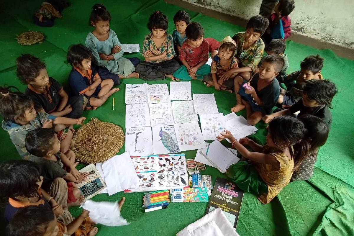 Young Chepang children sit cross-legged inside a modest classroom, gathered around various learning materials.