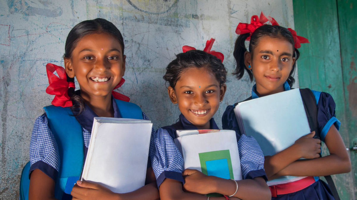 Indian rural schoolgirls holding books standing in school.