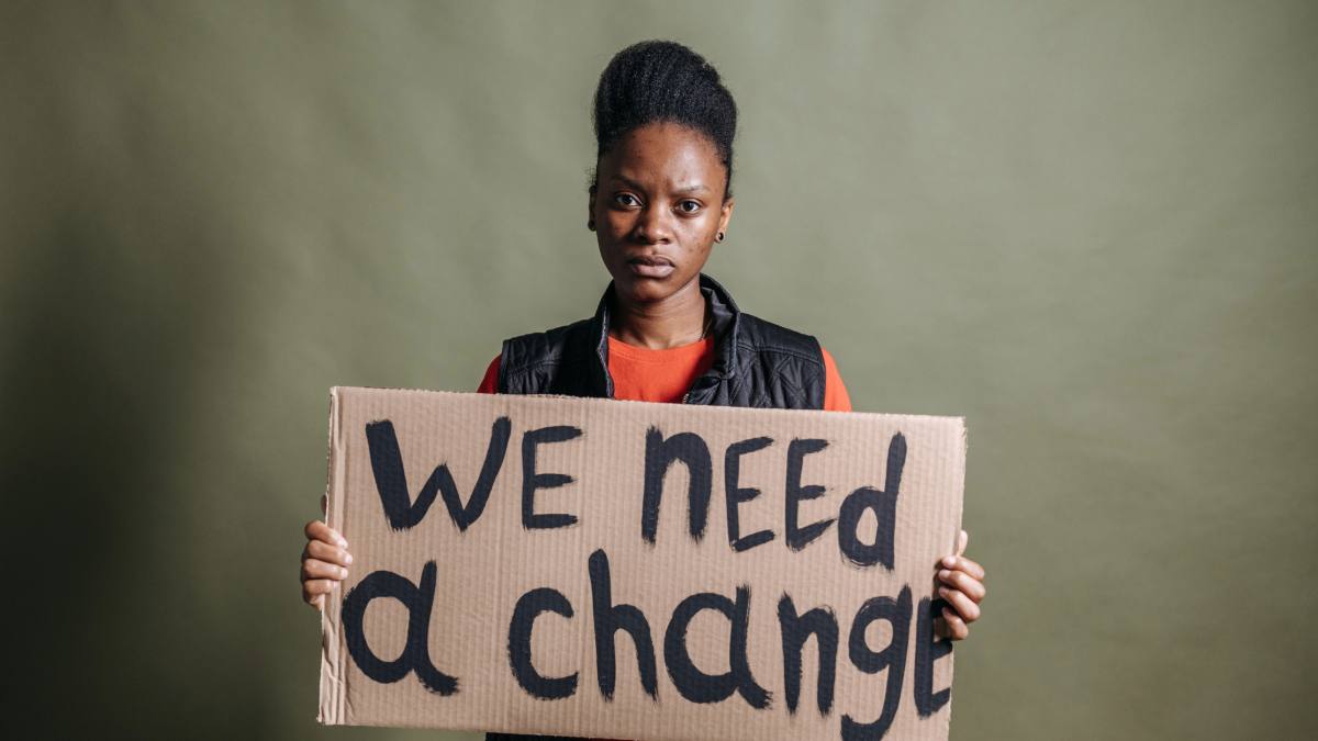 A woman holds a placard with the words 'We need a change.'