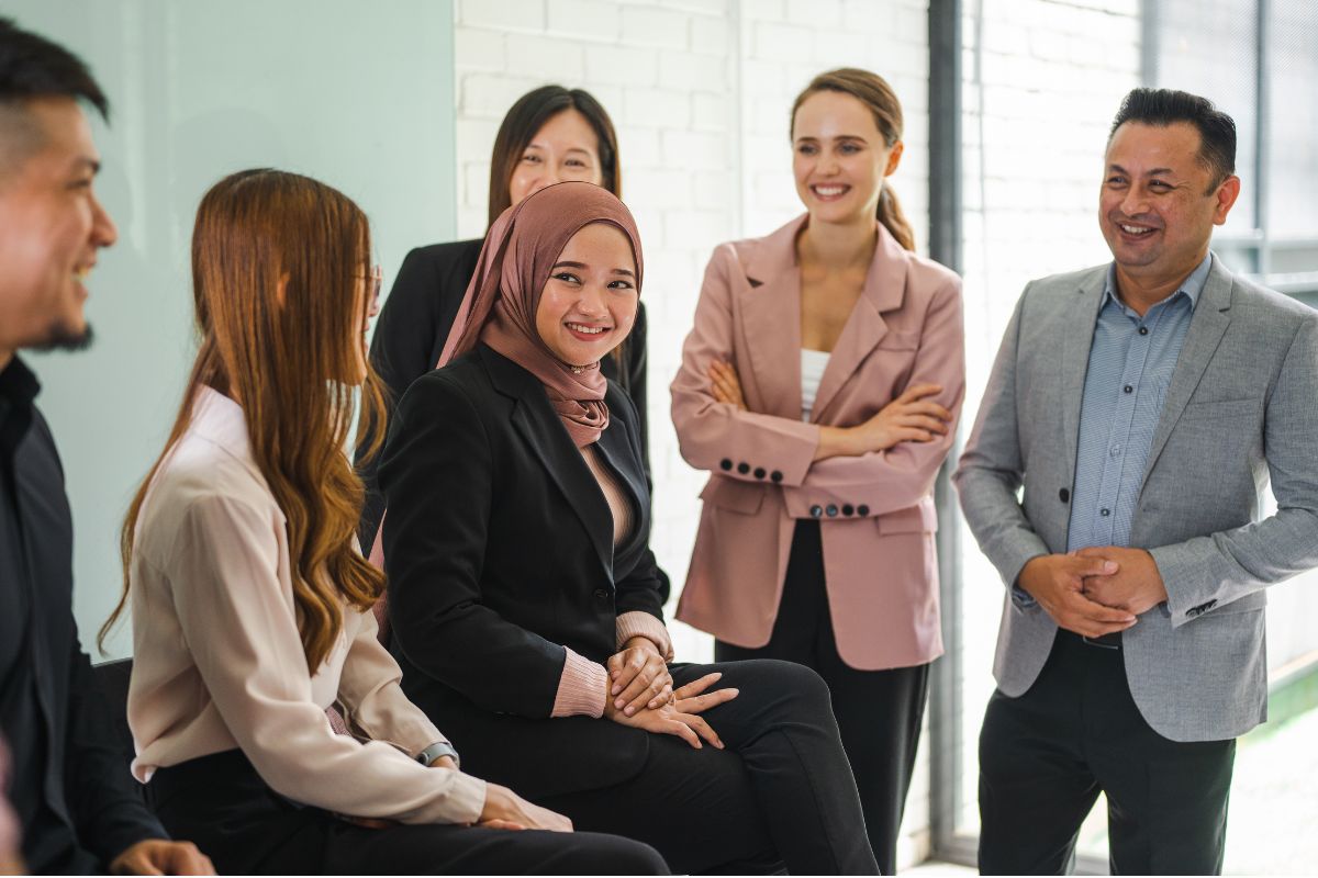A diverse group of professionals smiling in a modern office, reflecting workplace diversity in Malaysia.